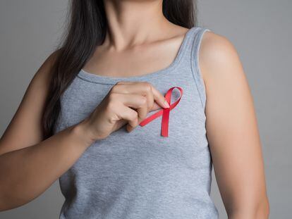 Closeup woman hand holding red ribbon HIV, world AIDS day awareness ribbon. Healthcare and medicine concept.