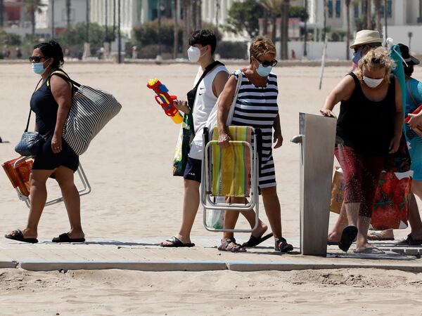 GRAFCVA6760. VALENCIA, 19/07/2020.- Varias personas, protegidas con mascarillas, acceden hoy a la playa de la Malvarrosa de Valencia, donde ayer se impuso la obligatoriedad del uso de las mascarillas en todos los espacios públicos.EFE/ Juan Carlos Cárdenas