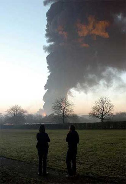Dos personas contemplan asombradas una enorme columna de humo negro.