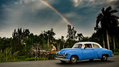 Un coche clásico estadounidense y un carro tirado por un caballo en una carretera de Cuba.