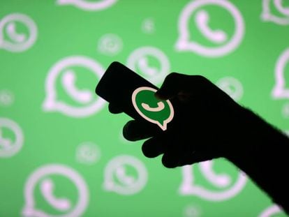 Un hombre con un móvil posa frente a una pantalla con el logo de WhatsApp.
 