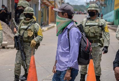 Un integrante de la autodefensa El machete camina frete a miembros del Ejército mexicano.