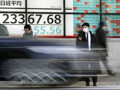 Un hombre mira el móvil delante de un monitor con información de la bolsa en Tokio. 