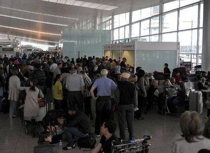 Cientos de pasajeros esperan en largas colas en los pasillos del aeropuerto de Barajas.