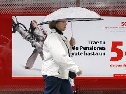 Una mujer camina frente a una sucursal bancaria en la que se anuncian planes de pensiones.