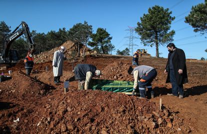 Un familiar y un empleado municipal entierran a una víctima de la COVID-19 en el cementerio de Baklaci (Estambul) el pasado 23 de noviembre, mientras las excavadoras abren nuevas tumbas para los fallecidos por la epidemia.