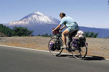 Una turista viaja en bicicleta por una carretera de Tenerife, con el volcán Teide al fondo.