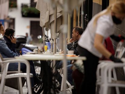 Una camarera de una cafetería de Santa Cruz de Tenerife limpia una mesa mientras varios clientes toman sus consumiciones.