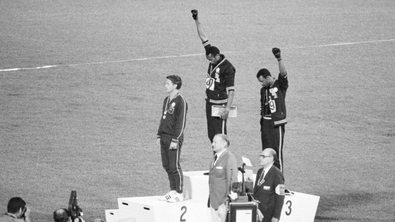 Los corredores estadounidenses Tommie Smith (centro) y John Carlos (derecha) levantaban sus puños con guantes negros en el podio de los Juegos Olímpicos de México de 1968 mientras sonaba el himno nacional estadounidense.