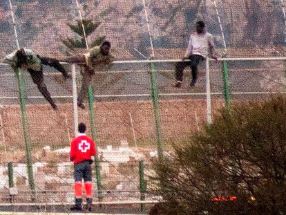Un miembro de Cruz Roja ayuda a tres de los inmigrantes que se han quedado este lunes subidos en la valla de Melilla.