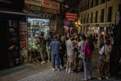 Varias personas hacen cola en una tienda de alimentación del centro de Madrid pasadas las doce de la noche.