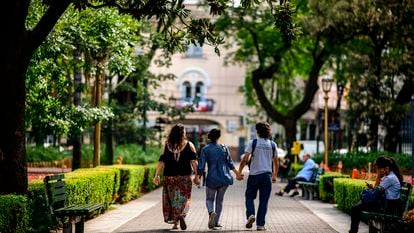 Tres jóvenes pasean por un parque cogidos de las manos.