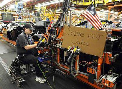 Un empleado de General Motors ensambla partes de un Corvette ante un cartel en el que pide que se salven los puestos de trabajo.