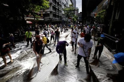 Decenas de escolares y adultos realizan operaciones de limpieza en una calle del centro de Bangkok.