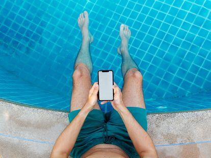 Uh hombre sostiene su móvil en la piscina.