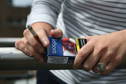 Un hombre fumando con una cajetilla de tabaco en las manos con los mensajes del daño que fumar causa a la salud.