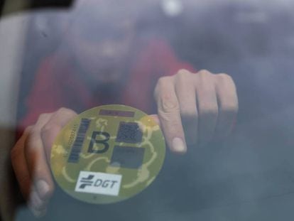 Un hombre coloca la etiqueta ambiental amarilla de la DGT en la luna de su coche.
