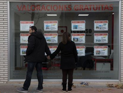 Dos jóvenes miran un escaparate con anuncios de pisos en el Ensanche de Vallecas (Madrid).