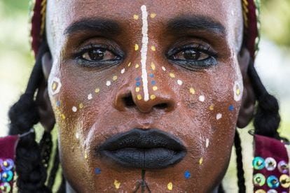 Un hombre wodaabe muestra su intrincado maquillaje para la fiesta nocturna. Usa todo lo que encuentra: ocre rojo del suelo para pintarse la cara de naranja y una pasta hecha de tiza para resaltar la simetría de sus facciones. La línea de los ojos y el color de labios los obtiene con huesos de garza carbonizados o con ácido de batería. A una parte del maquillaje se le atribuyen poderes mágicos y los wodaabes hacen todo lo posible por obtenerlo. El polvo de color anaranjado para el rostro se obtiene cerca de una montaña especial próxima a Jongooria, en el centro de Níger, y algunos clanes de wodaabes emprenden un viaje de ida y vuelta de 1.400 kilómetros para aprovisionarse.