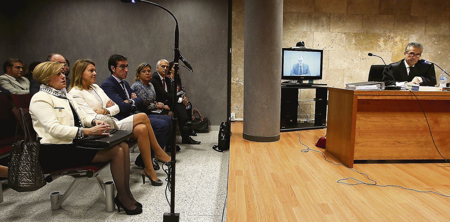 Dolores de Cospedal, en el centro de la primera fila de la sala de vistas, escucha, sin mirar al monitor, la respuesta de Bárcenas a través de videoconferencia desde la cárcel, en 2013.