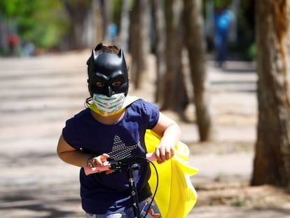 Una niña protegida con mascarilla y una careta de Batman juega con su patinete en la calle. 