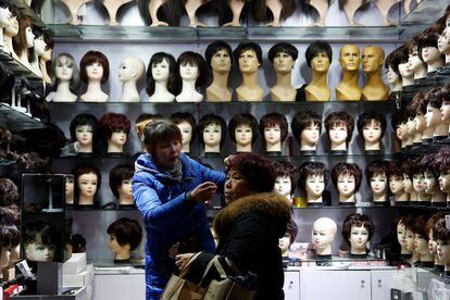 Una vendedora ayuda a una clienta a colocarse la peluca en una tienda cerca de la estación de tren de Shanghai (China).