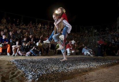 Un hombre, llevando a cuestas a una chica, pasa sobre la alfombra de brasas de leña en el ritual que se celebra cada año en San Pedro Manrique (Soria).