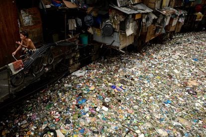 Un hombre sentado en una bicicleta junto a un río lleno de basura en Manila (Filipinas).