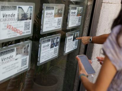 Dos personas observan varios anuncios de venta de viviendas en un escaparate de una inmobiliaria, en Madrid.