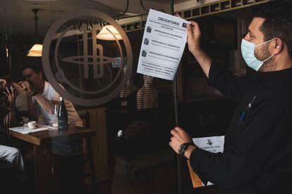 Un camarero de un restaurante de Santiago de Compostela retira un cartel con medidas contra la covid, en agosto.