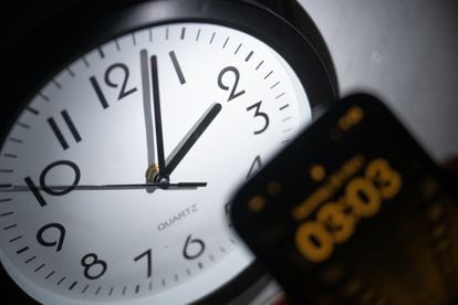 Un reloj analógico junto a un teléfono móvil que marca la hora.