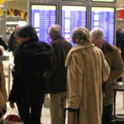 Varios viajeros miran los paneles de información de sus vuelos en la terminal 4 del aeropuerto de Barajas (Madrid)