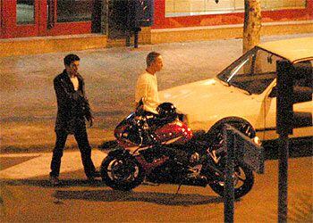 El atracador, con ropa oscura, camina detrás del rehén hacia la moto en la que intentó huir.