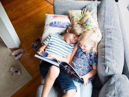 Dos hermanos se divierten leyendo en el sofá.