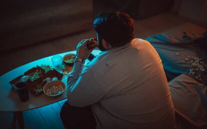 Un hombre comiendo una hamburguesa delante de la televisión. 