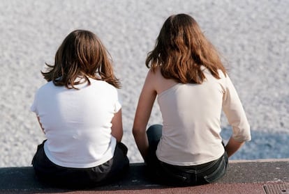 Dos chicas, sentadas en un paseo marítimo.
