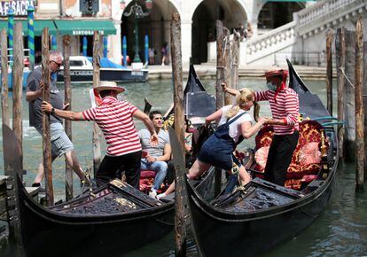 Gondoleros ayudan a varios turistas a subir a sus embarcaciones en un canal de Venecia.