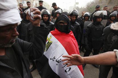 Un manifestante femenina, con el rostro cubierto y envuelta en la bandera egipcia, se interpone entre la policía y los manifestantes.