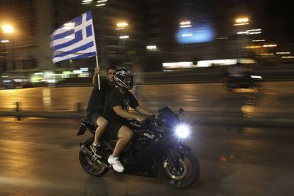 Dos seguidores griegos recorren las calles de Atenas en moto con una bandera de su país, que hoy acude a las urnas.