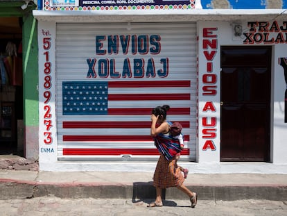 Una mujer pasa con su hijo frente a un local de envíos hacia y desde EE UU en Joyabaj (Guatemala).