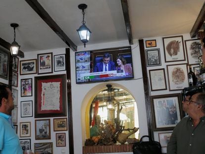 La gente ve a Pedro Sánchez y Carmen Calvo, en una pantalla de televisión durante el debate de investidura en el Parlamento, en un bar en Ronda. 