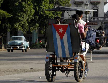 Un hombre lleva a dos personas en su carro adornado con la bandera cubana en La Habana.