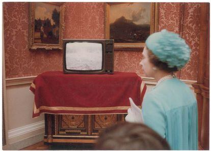 La reina Isabel II al lado de un televisor que tiene en pantalla la retransmisión en directo de la boda.