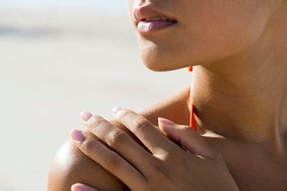 Woman touching bare shoulder at the beach, cropped