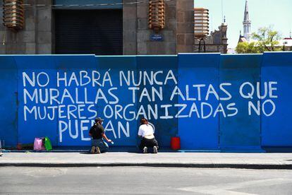 Dos mujeres pintan sobre una valla a las afueras del Banco de México, el Gobierno ha hecho el despliegue alrededor de comercios y edificios públicos por distintas calles del centro histórico, como la avenida Juárez y la calle 5 de mayo. 