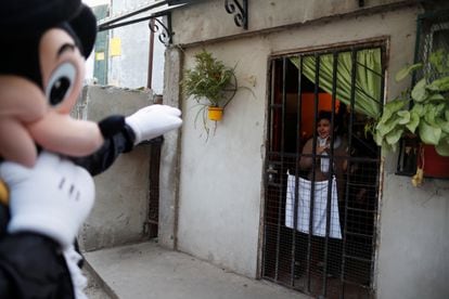 Un voluntario disfrazado como Mickey Mouse saluda a una niña encerrada en su casa en Fuerte Apache, Buenos Aires, en agosto de 2020.