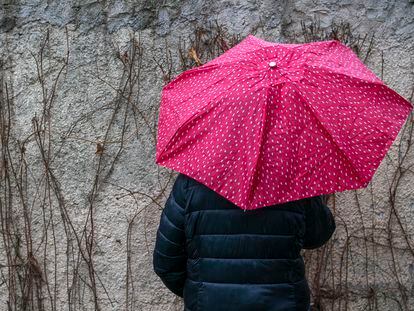 Sandra (nombre figurado) esconde su rostro tras un paraguas un día de lluvia en un municipio de la Comunidad de Madrid.