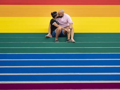 Una pareja se besa sobre una gran bandera gay instalada en Roosevelt Island, Nueva York.