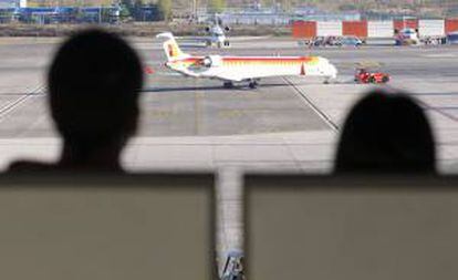 En la imagen, dos personas observan uno de los aviones de Iberia en la T 4 del aeropuerto madrileño de Barajas. EFE/Archivo