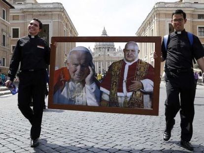 Dos sacerdotes caminan por la Plaza de San Pedro con un collage de los dos papas que serán canonizados el 27 de abril de 2014.